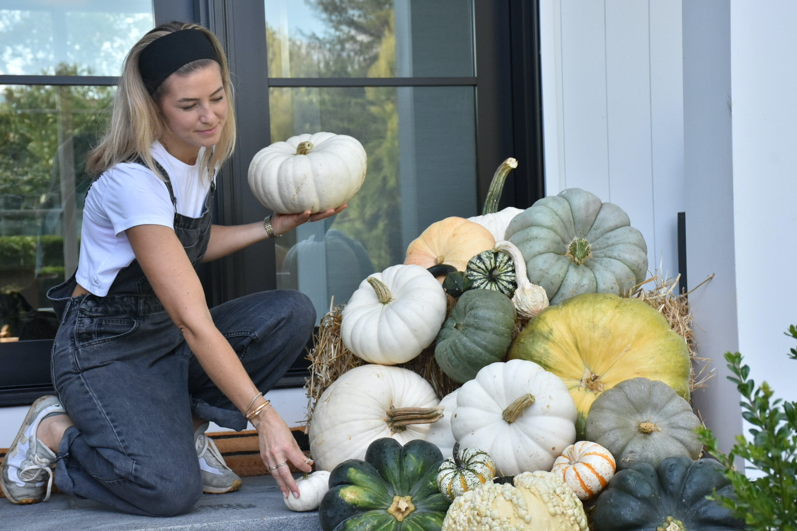 Woman holding a white pumpkin among various pumpkins on a porch.