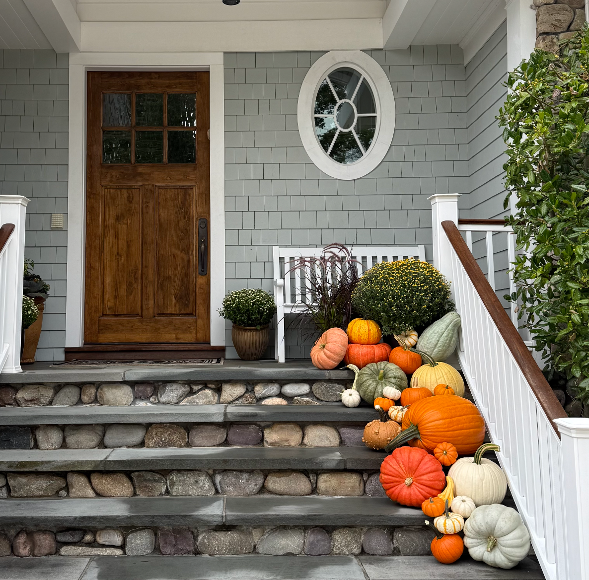 Front porch with decorative pumpkins and gourds on stone steps, wooden door, and gray wall in Connecticut
