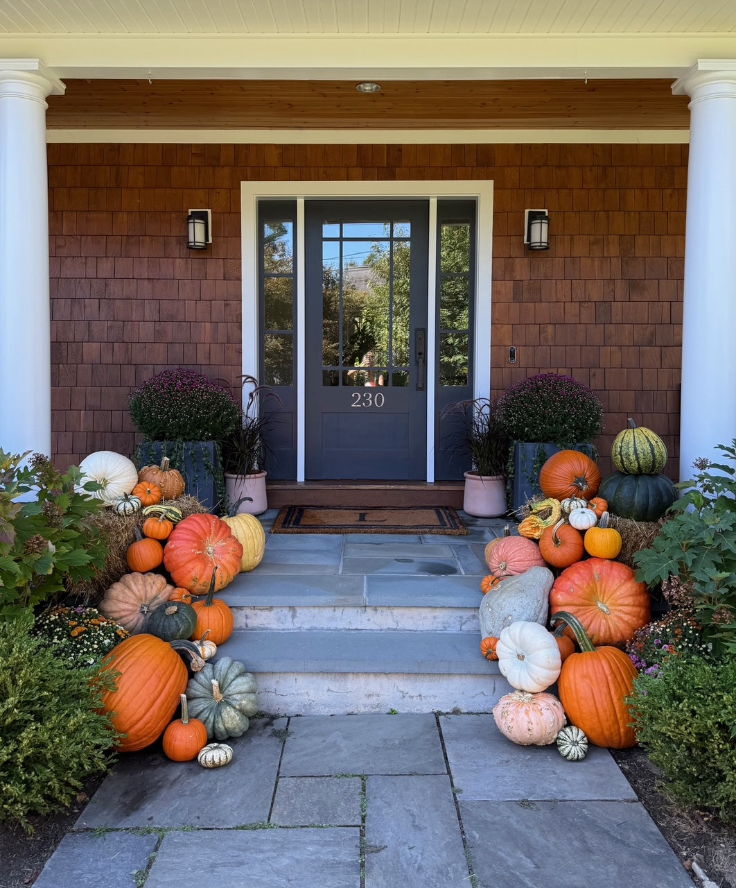 Fall autumn porch pumpkins and gourds on a stone porch in front of a house with a brown exterior in Westport Fairfield County CT Connecticut